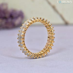 May include: A gold eternity ring with a continuous row of rectangular-cut diamonds. The ring's band is a warm gold color, and the diamonds are clear and sparkling. The ring is a classic piece of jewelry.