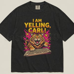 May include: Black t-shirt with a graphic of an angry orange tabby cat yelling at a keyboard. The text "I AM YELLING, CARL!" is in yellow and pink. The cat is surrounded by pink lightning bolts.