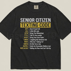 May include: Black t-shirt with the text "SENIOR CITIZEN TEXTING CODE" in white and yellow. The shirt lists common texting acronyms and their meanings, such as "BFF" for "Best Friend Fell" and "LOL" for "Little Old Lady."