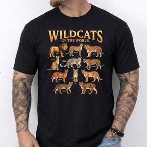 May include: Black t-shirt featuring the text "WILDCATS OF THE WORLD" in gold lettering above illustrations of various wild cat species, including lions, tigers, and cheetahs. The shirt is a crew neck style.