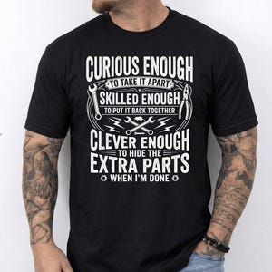 May include: Black t-shirt with white text that reads "CURIOUS ENOUGH TO TAKE IT APART, SKILLED ENOUGH TO PUT IT BACK TOGETHER, CLEVER ENOUGH TO HIDE THE EXTRA PARTS WHEN I'M DONE." The design includes wrench and pliers graphics.