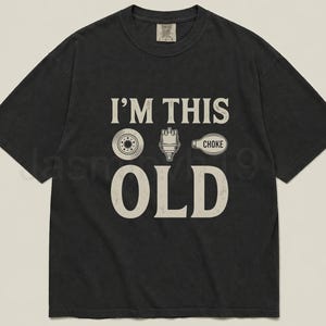 May include: Black t-shirt with the text "I'M THIS OLD" and illustrations of a tire, spark plug, and choke. The shirt has a vintage, worn look.