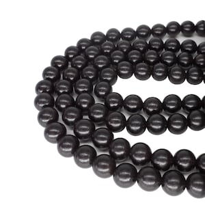 Könnte beinhalten: Nahaufnahme einer Kette aus dunkelbraunen Holzperlen. Die Perlen sind rund und haben eine glatte, polierte Oberfläche. Die Perlen sind aufgefädelt und bilden eine Halskette oder ein Armband. Der Hintergrund ist schlicht weiß.
