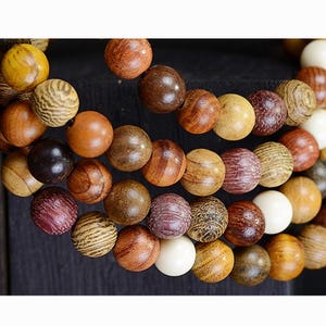 Può includere: Primo piano di un braccialetto di perline con una varietà di perline di legno nei toni del marrone, beige e crema. Le perline hanno diverse trame e motivi, alcune lisce e altre con venature del legno.