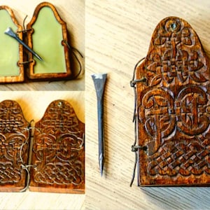 Könnte beinhalten: Hölzerne Buchdeckel mit aufwendigen Schnitzereien, zusammen mit einem Metallwerkzeug. Die Deckel sind mit Bindfäden verbunden. Ein Satz hat eine grüne Innenseite, der andere ist aus massivem Holz. Das Werkzeug ist dunkelmetallfarben.