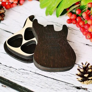 Könnte beinhalten: Zwei gitarrenförmige Holztabletts, eines dunkelbraun und das andere hellbraun mit drei kreisförmigen Aussparungen. Die Tabletts liegen auf einer weißen Holzoberfläche, mit Tannenzapfen und roten Beeren im Hintergrund.