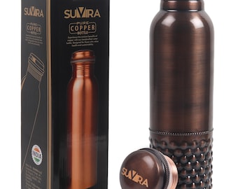 May include: A copper water bottle with a matching lid and a decorative base. The bottle is next to its original black box, which features the brand name "SUVIRA" and the words "Pure Copper Bottle."