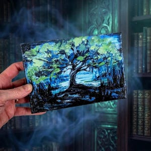May include: An original acrylic painting of a tree in a forest. The artwork features a large tree with a dark trunk and green and blue foliage. The background is a dark blue and black, creating a moody and atmospheric scene. The painting is on a small, square canvas.