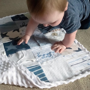May include: A patchwork baby blanket in shades of blue and white, featuring star and striped patterns. The blanket has a white, textured border. The text "I love my sunshine" is embroidered on one of the patches.