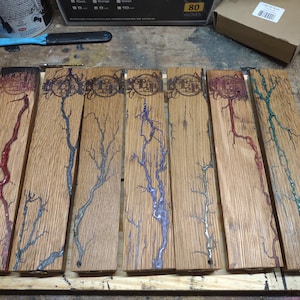 May include: A collection of wooden planks with a lightning bolt design. Each plank is a light brown color with a unique colored resin design in red, blue, purple, and green. The planks have a dark border and a circular logo.