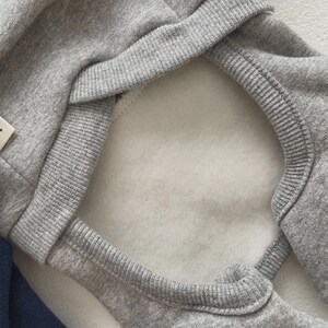 May include: Close-up of a gray hooded sweatshirt with a white fleece lining. The hood's edge and seams are ribbed. The sweatshirt is made of a soft, comfortable material.