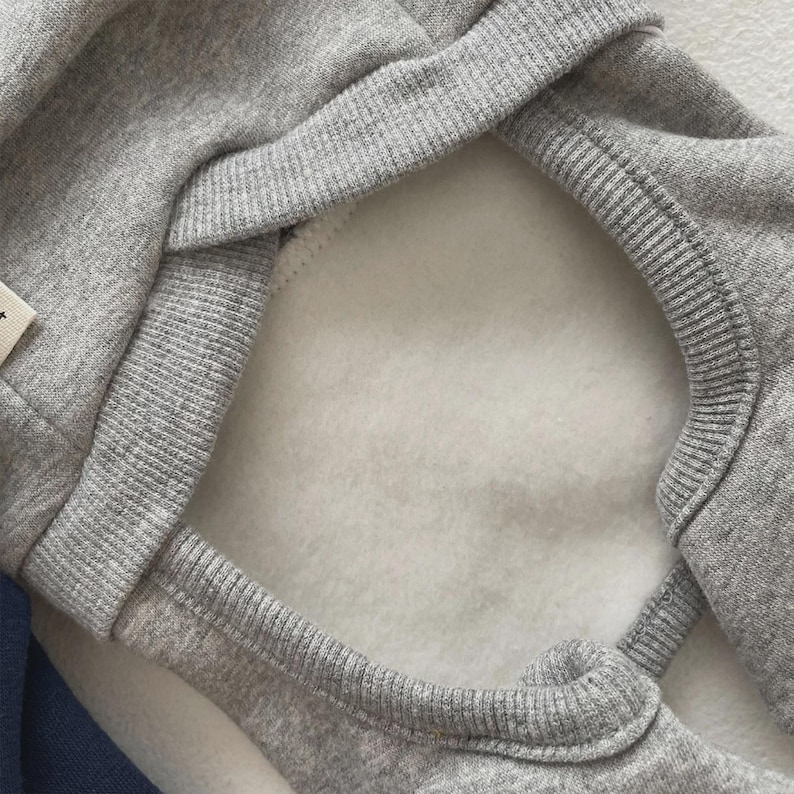 May include: Close-up of a gray hooded sweatshirt with a white fleece lining. The hood's edge and seams are ribbed. The sweatshirt is made of a soft, comfortable material.
