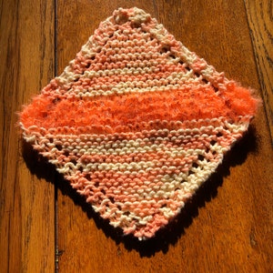 May include: A knitted dishcloth with a pink and white striped pattern and a fuzzy orange border.