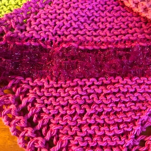 May include: A pink knitted dishcloth with a sparkly pink trim. The dishcloth is made with a simple knit stitch.