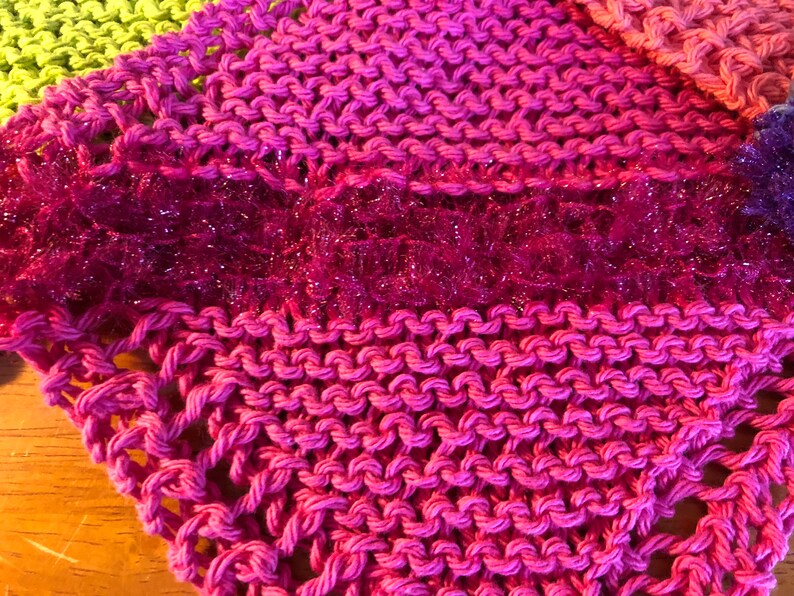 May include: A pink knitted dishcloth with a sparkly pink trim. The dishcloth is made with a simple knit stitch.