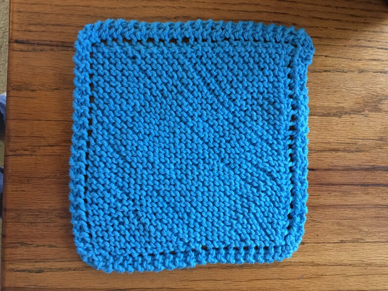 May include: A bright blue knitted dishcloth with a simple stitch pattern and a white border.