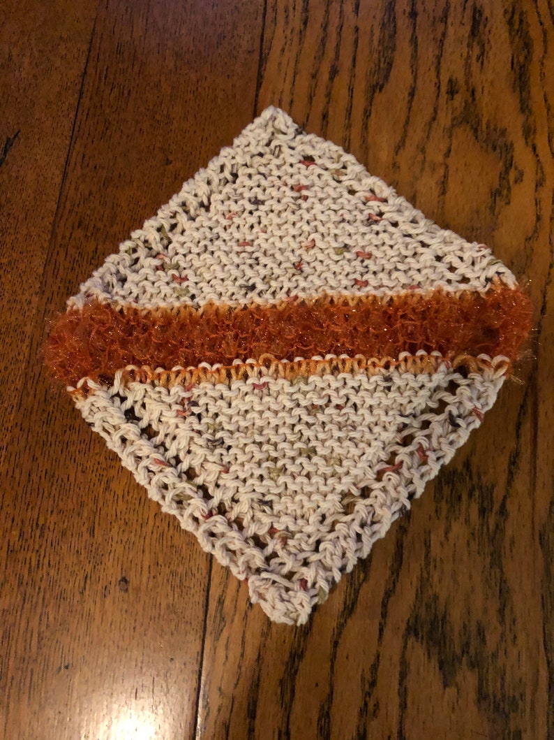 May include: A white knitted dishcloth with a brown and orange sparkly trim.