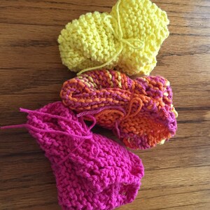 May include: Three knitted dishcloths in different colors: pink, orange and yellow. The dishcloths are made with a simple stitch and have a textured look.
