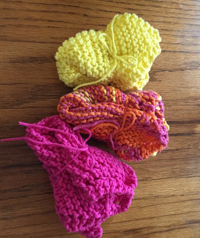 May include: Three knitted dishcloths in different colors: pink, orange and yellow. The dishcloths are made with a simple stitch and have a textured look.