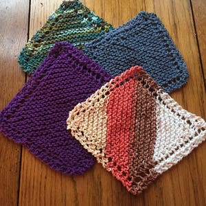 May include: Four knitted dishcloths in different colors and patterns. The dishcloths are purple, blue, green, and a multi-colored stripe pattern.