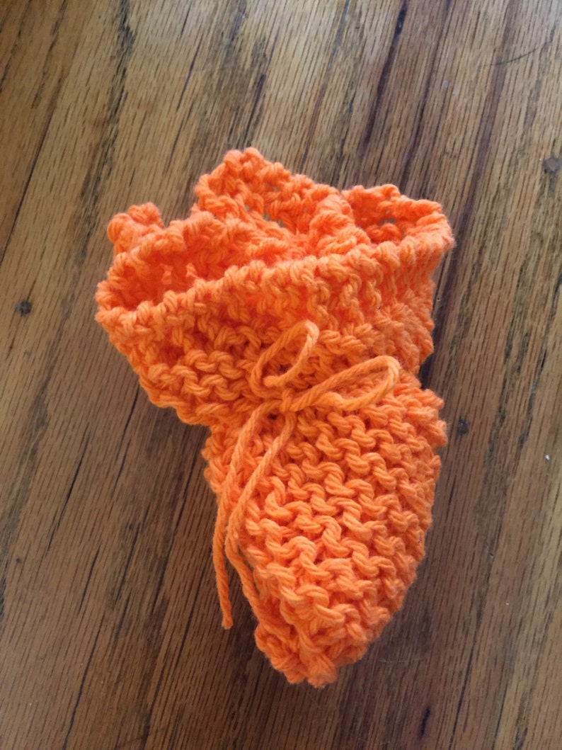 May include: A bright orange knitted dishcloth with a tied string in the center.