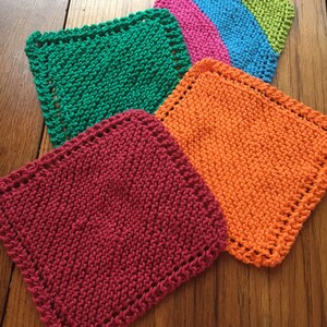 May include: Four knitted dishcloths in different colors: green, pink, orange, and red. The dishcloths are square and have a decorative border.