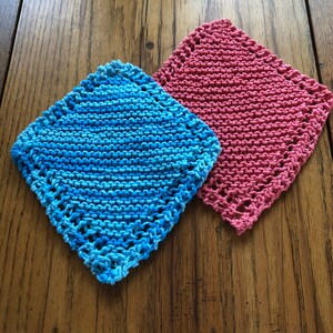 May include: Two knitted dishcloths, one blue and one pink, on a wooden surface.