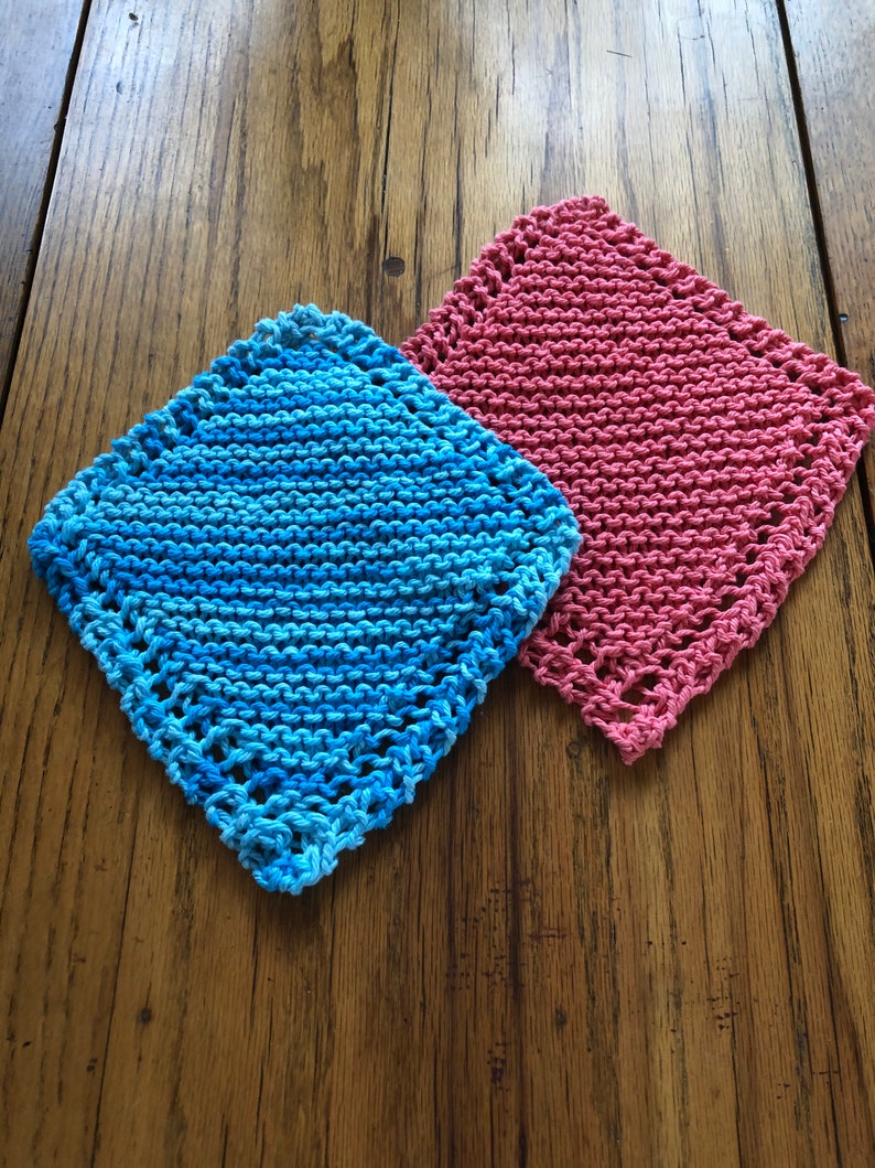 May include: Two knitted dishcloths, one blue and one pink, on a wooden surface.