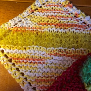 May include: A multi-colored knitted dishcloth with a yellow, orange, and white striped pattern. The dishcloth has a textured, fluffy surface.