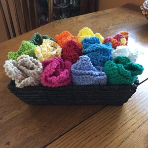 May include: A basket filled with colorful crocheted dishcloths in various shades of green, yellow, orange, red, pink, blue, and white.