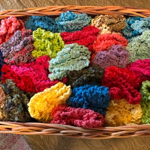 May include: A wicker basket filled with colorful crocheted scrubbies. The scrubbies are in various shades of blue, green, red, yellow, and brown.
