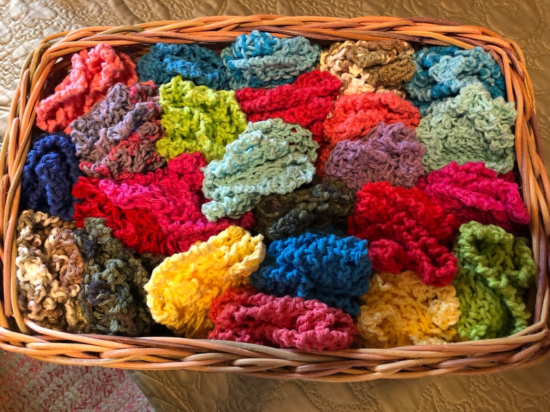May include: A wicker basket filled with colorful crocheted scrubbies. The scrubbies are in various shades of blue, green, red, yellow, and brown.