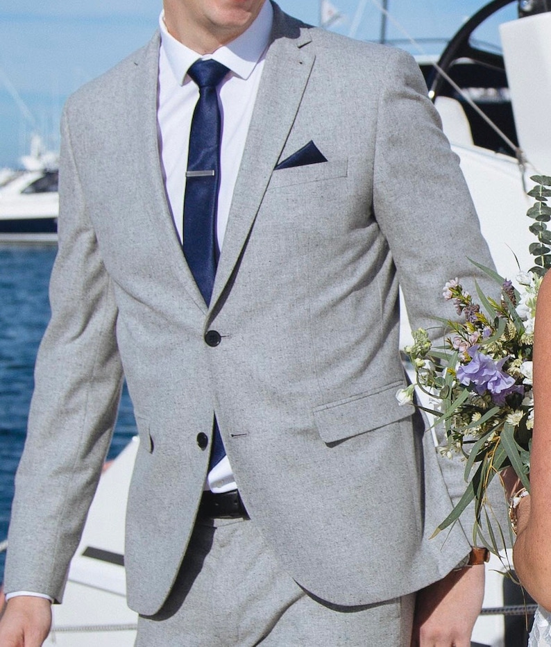 Model in suit and tie wears antique silver tie clip on dark blue tie. The darkened silver tie clip looks elegant and complements the grey suit and blue tie perfectly.