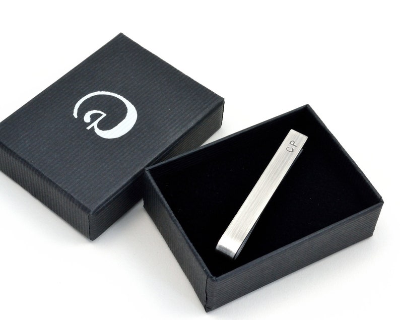 Oxidised Sterling silver tie clip shown in elegant black gift box with black interior as it will arrive when purchased. Box has simple logo in silver on front and fits the tie clip perfectly. Tie clip is shown personalised with initials on front.