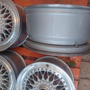 Puede incluir: Un juego de llantas de aleaci&oacute;n de color plateado con un dise&ntilde;o de m&uacute;ltiples radios. Las llantas tienen un acabado met&aacute;lico y est&aacute;n dispuestas sobre un palet de madera. Las tapas centrales muestran el logotipo "BBS".