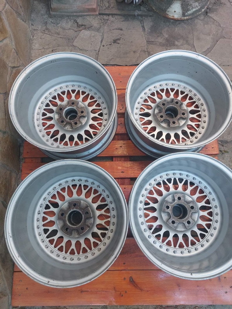 Puede incluir: Cuatro llantas de aleaci&oacute;n de plata para coche con un dise&ntilde;o de radios m&uacute;ltiples. Las ruedas tienen un patr&oacute;n circular de peque&ntilde;os agujeros alrededor del centro y est&aacute;n sobre una superficie de madera. Las ruedas est&aacute;n dise&ntilde;adas para un coche.