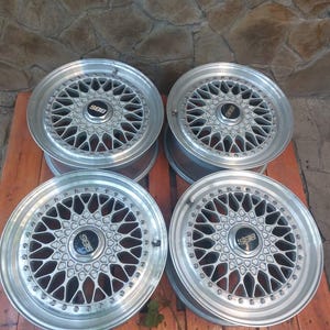 Puede incluir: Cuatro llantas de aleaci&oacute;n plateadas con un dise&ntilde;o de radios m&uacute;ltiples. Cada llanta presenta un buje central con el logotipo "BBS" en negro. Las llantas est&aacute;n dispuestas sobre un palet de madera, mostrando su intrincado dise&ntilde;o y acabado met&aacute;lico.