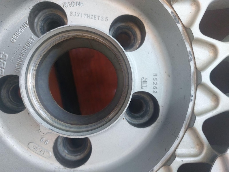 Puede incluir: Primer plano de una llanta de coche plateada con m&uacute;ltiples orificios para pernos. La llanta tiene el texto "GERMANY" y "RS 262" impreso. El centro de la rueda tiene una gran abertura circular.