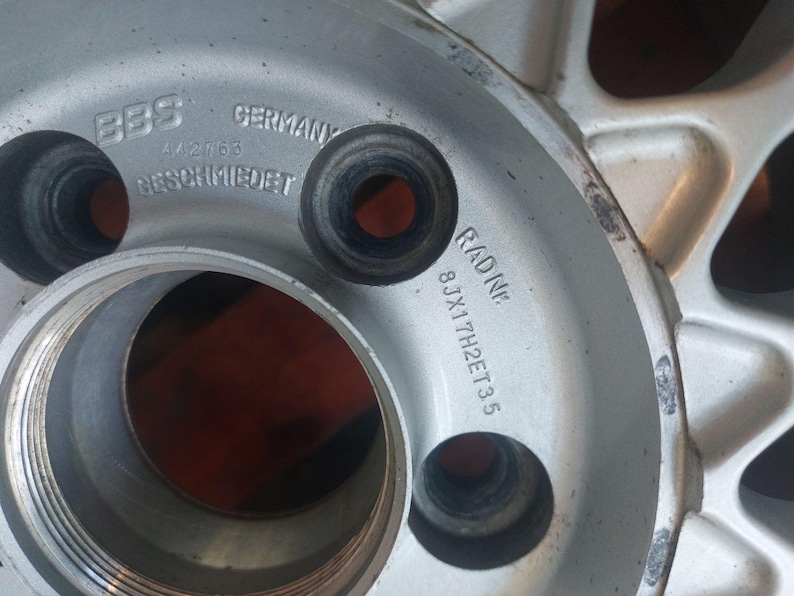 Puede incluir: Primer plano de una llanta BBS plateada. La llanta tiene varios agujeros y se ven los textos "BBS GERMANY" y "RADINE 8JX17H2ET35". La llanta parece ser de metal.