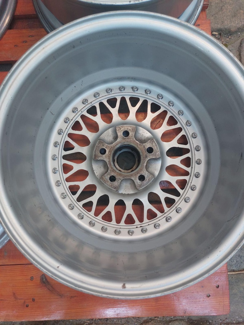 Puede incluir: Una llanta de coche plateada con un dise&ntilde;o de m&uacute;ltiples radios. La llanta tiene una llanta circular con una serie de peque&ntilde;os pernos alrededor del borde. El centro de la llanta presenta un cubo con m&uacute;ltiples orificios para pernos.