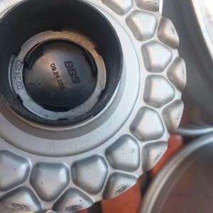 Puede incluir: Primer plano de un tapacubos plateado con un patr&oacute;n geom&eacute;trico. La tapa tiene el logotipo de BBS y los n&uacute;meros 09.24.036. La rueda es parcialmente visible en el fondo.