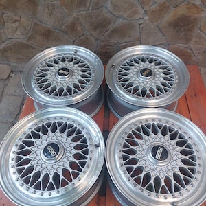 Puede incluir: Cuatro llantas de aleaci&oacute;n BBS de color plateado. Cada rueda presenta un dise&ntilde;o de radios m&uacute;ltiples con un buje central con el logotipo de BBS en negro. Las ruedas est&aacute;n dispuestas sobre un pal&eacute; de madera contra una pared de piedra.