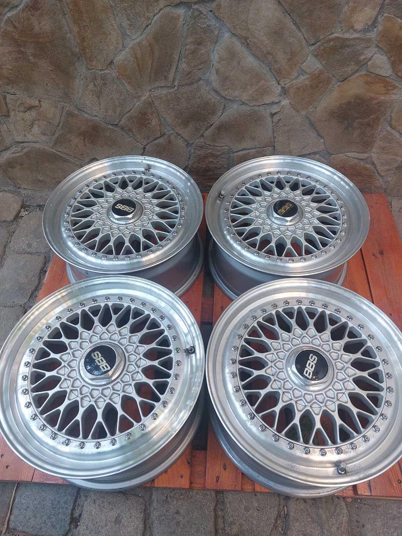 Puede incluir: Cuatro llantas de aleaci&oacute;n BBS de color plateado. Cada rueda presenta un dise&ntilde;o de radios m&uacute;ltiples con un buje central con el logotipo de BBS en negro. Las ruedas est&aacute;n dispuestas sobre un pal&eacute; de madera contra una pared de piedra.