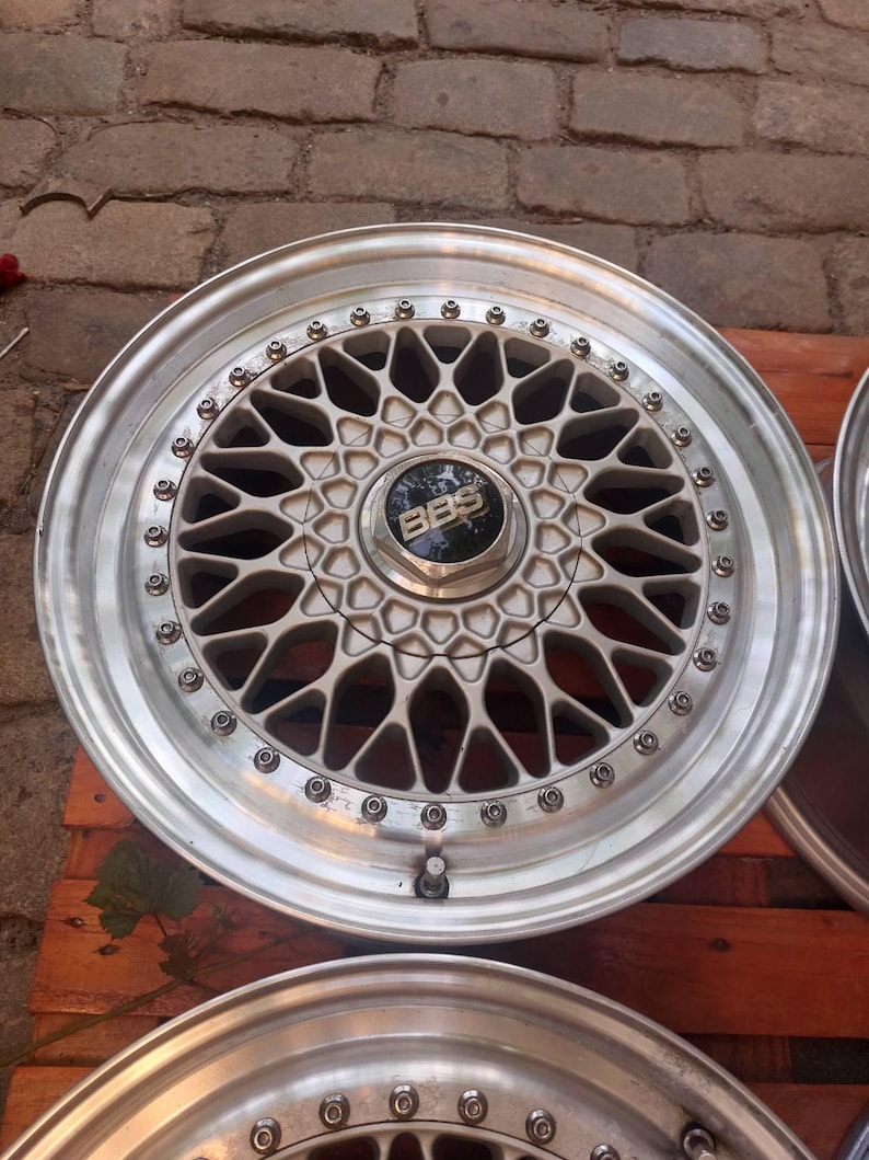 Puede incluir: Llanta de coche plateada con un dise&ntilde;o de radios geom&eacute;trico complejo. La tapa central presenta el logotipo "BBS" en negro. La llanta tiene un acabado met&aacute;lico pulido. El di&aacute;metro de la llanta es de aproximadamente 38 cm, para uso automotriz.