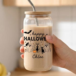 May include: A clear glass tumbler with a bamboo lid and a metal straw, filled with a beige beverage. The glass features black graphics of ghosts, cats, a bat, and a pumpkin, with the text "happy HALLOWEEN" and the name "Chloe" printed on it.