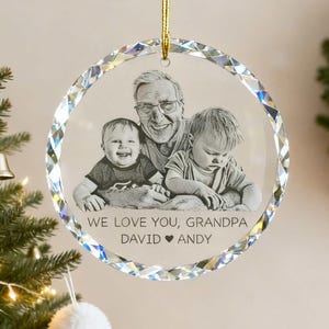 Op de afbeelding: Een heldere, ronde kristallen ornament met een gouden draad om op te hangen. Het ornament heeft een zwart-wit foto van een man en twee kinderen, met de tekst "WE LOVE YOU, GRANDPA DAVID ♥ ANDY".
