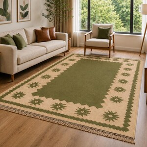 May include: A rectangular area rug featuring a solid olive green center panel surrounded by a wide beige border. The border is decorated with a repeating olive green star pattern and a jagged inner edge, finished with short fringe on both ends.