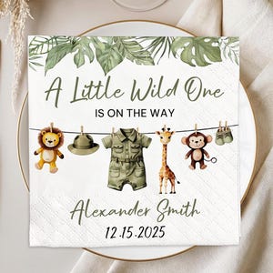 May include: A square white paper napkin with a jungle theme. The text "A Little Wild One Is On The Way" is printed on the napkin. The napkin has illustrations of a lion, hat, safari outfit, giraffe, monkey, and baby shoes.