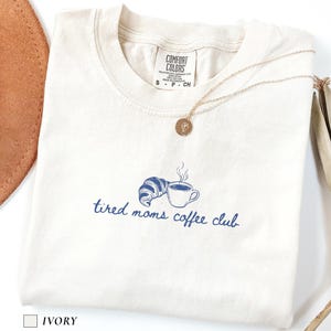 Minimalist comfort colors shirt with tired moms coffee club text and simple line art of coffee cup and croissant