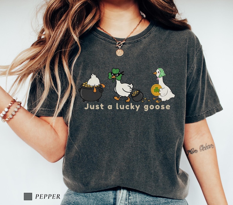 pepper comfort colors t-shirt with three illustrated geese, one in a pot of gold, one wearing a shamrock mask, and one holding a coin, playful st patrick’s day design